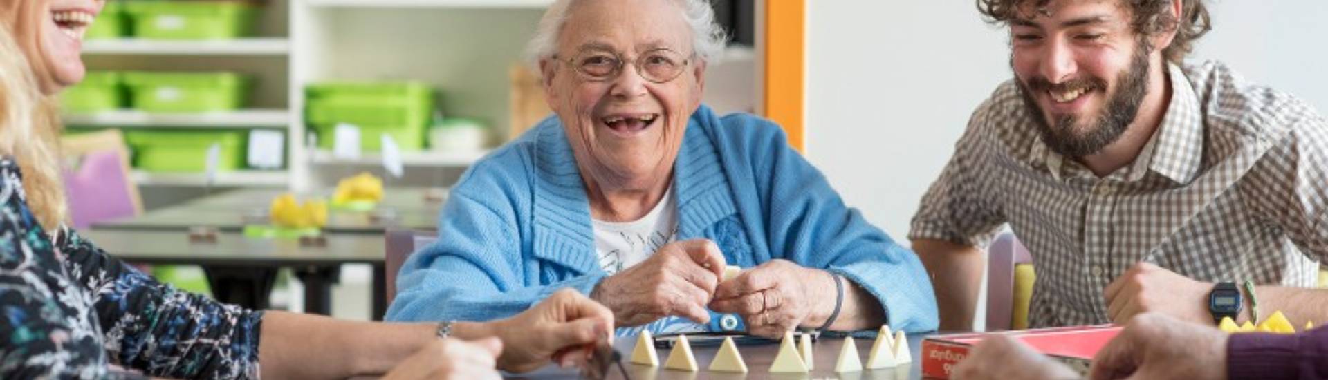personne âgée qui rigole et joue à un jeu de société avec un professionnel travaillant à l'accueil de jour