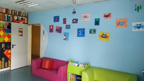 Salle du périscolaire du coin des mômes colorée avec des canapés et des dessins d'enfants accrochés sur les murs 