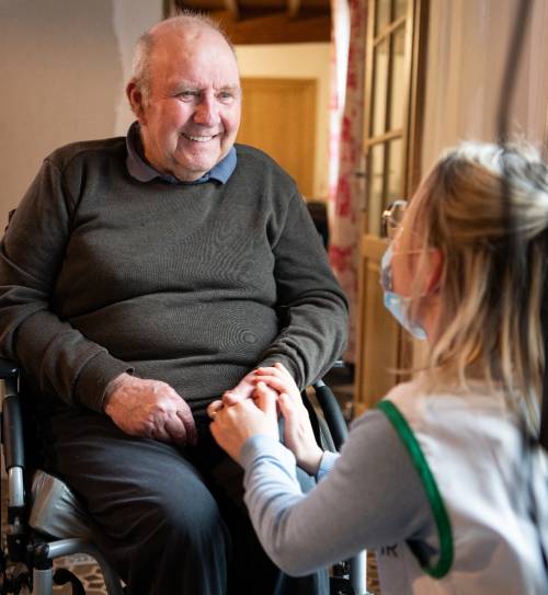 Aide-soignante qui se met à la hauteur de son patient et lui tient la main 