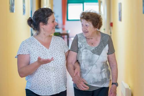 Professionnelle et personne aidée qui marchent ensemble dans un couloir 